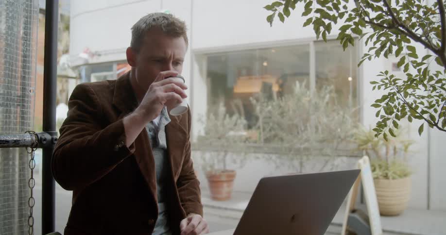Man sitting at the table uses laptop and sips his coffee in the coffee shop