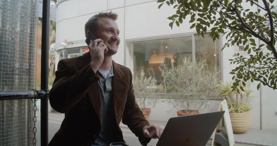 Man sitting at the table uses laptop and talks to someone on the smartphone in the cafe