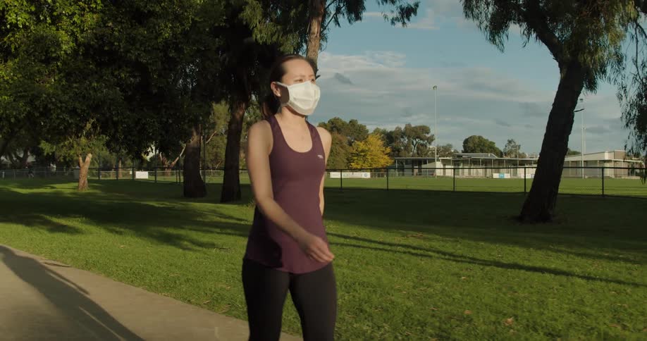 An asian woman strolls down a sidewalk while wearing a face mask