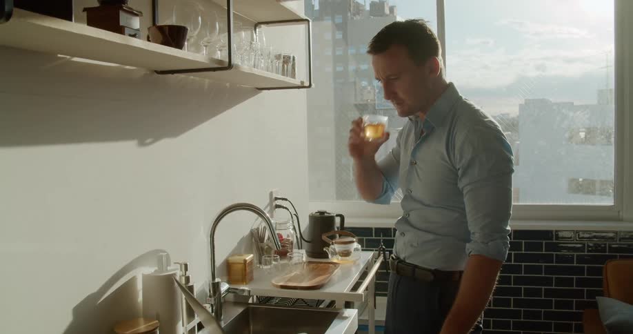 A man drinking while typing on a laptop resting on a counter next to the sink