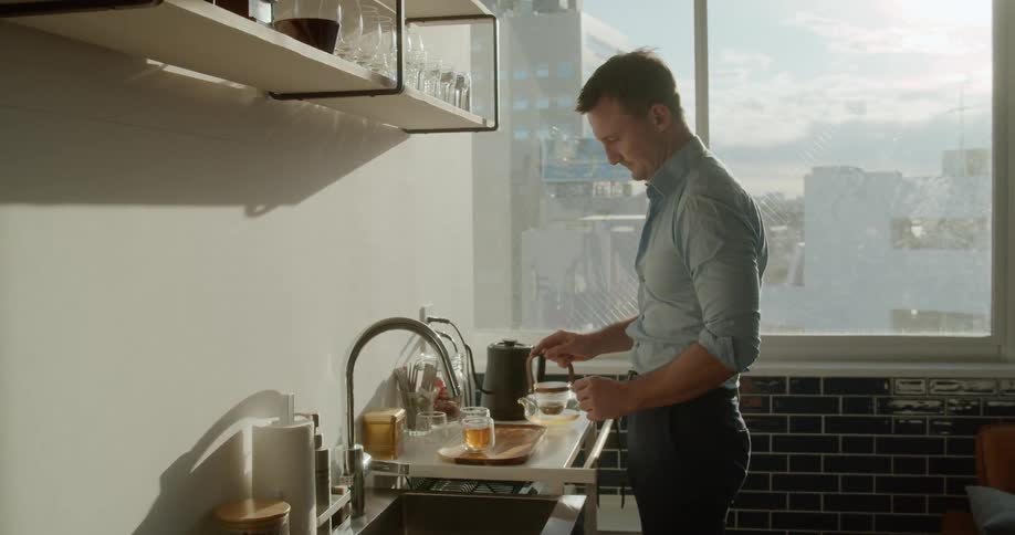 Man serving cup of tea over the kitchen in an apartment