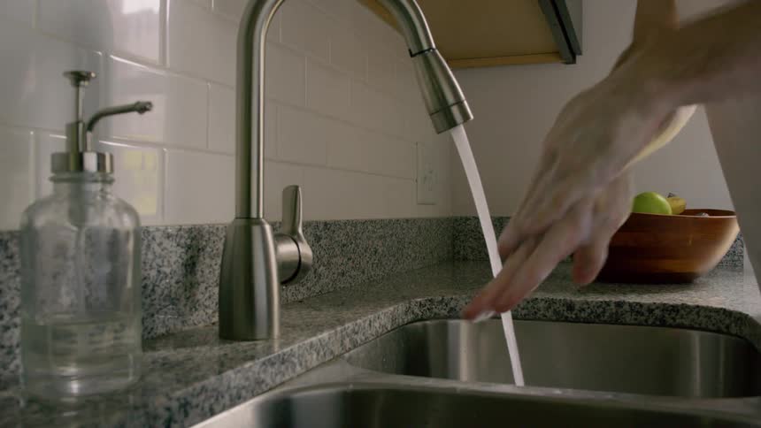 A man washes his hands in a kitchen sink