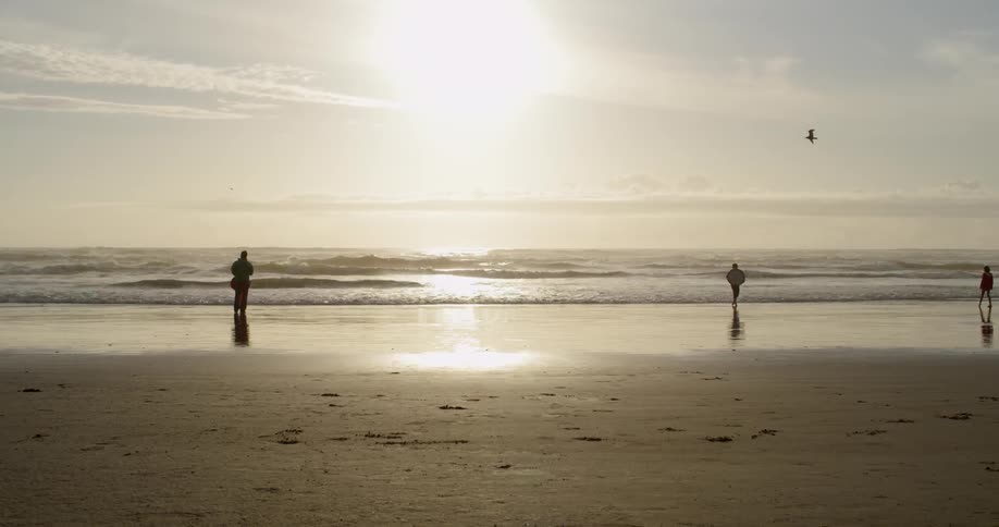 People are walking along the beach at sunset
