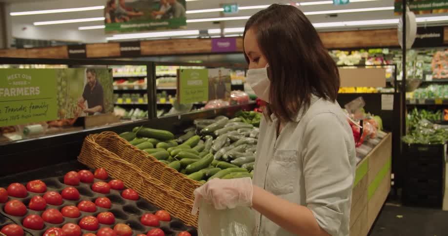 Asian woman wearing mask and gloves due to pandemic picking tomatoes in produce aisle