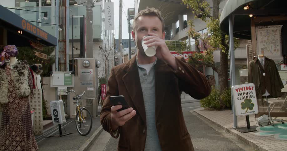 A man walks along drinking his coffee and looking at his phone