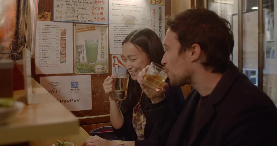 A man and woman toast before taking a drink at a restaurant counter