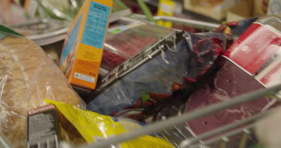Woman wearing a glove places a grocery item in a shopping cart