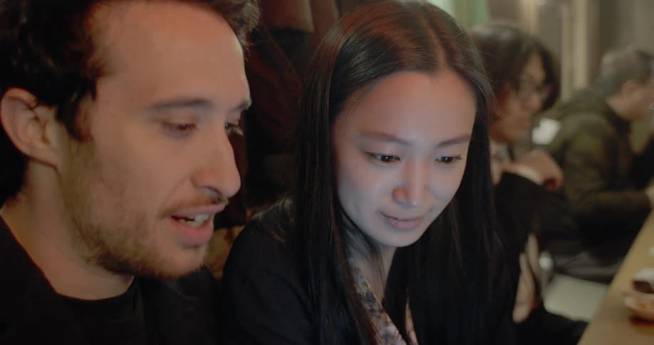 A man and a woman sitting at a table looking at a smart phone