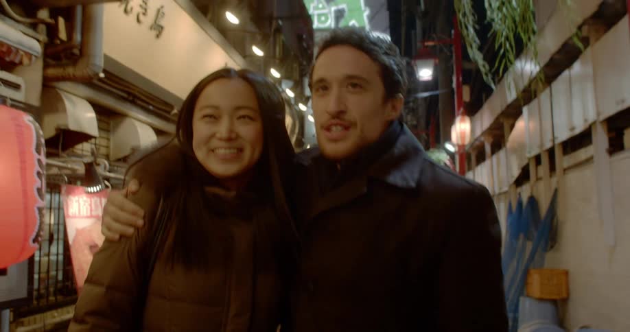 A man and woman walk down a street arm in arm then the man puts his arm around the woman
