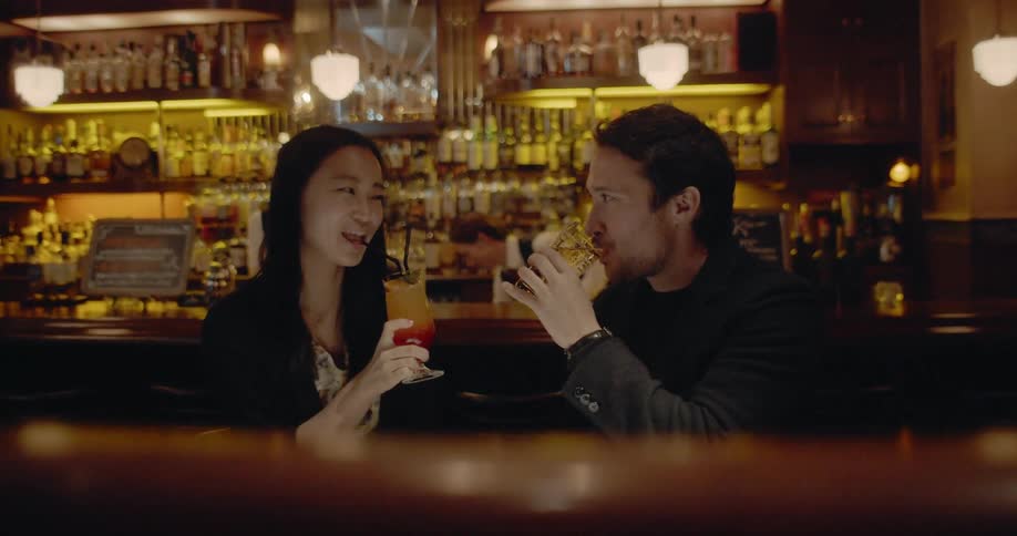 Asian woman and white man sitting at the table drink cocktails in the bar