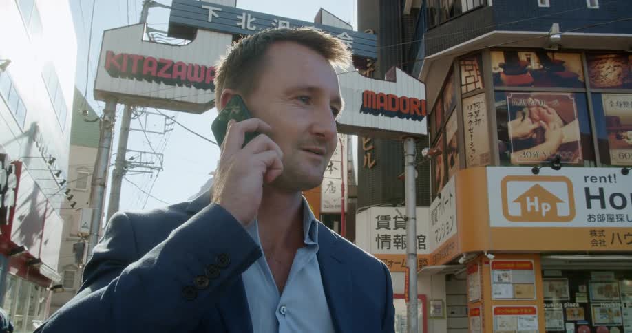 A man stands in front of a city building and talks on a cell phone