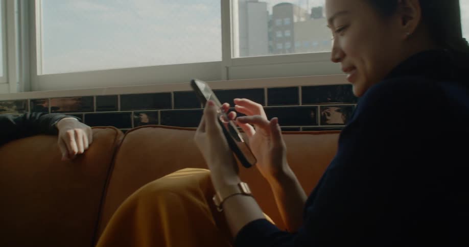 A man sitting on a sofa looking at a smartphone before returning it to a woman