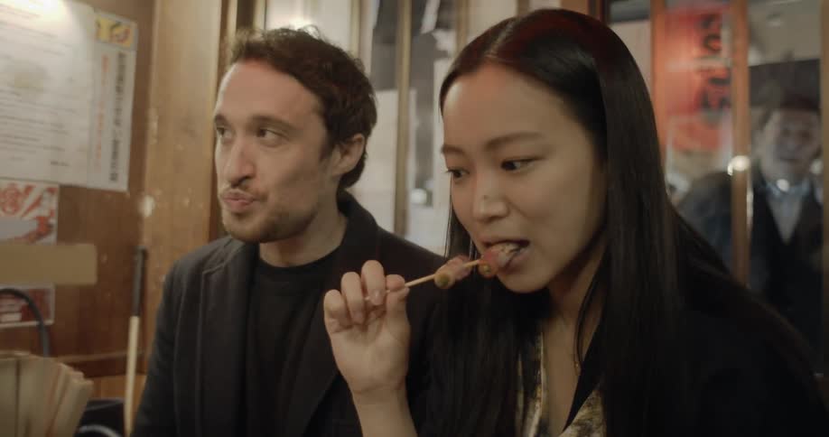 A woman takes a bite of food off of a kabob