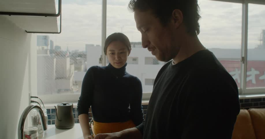 A white man fixes drinks while an asian woman watches and speaks with him