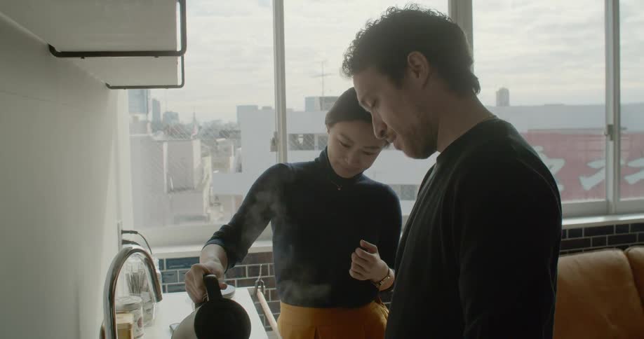 Man and woman in apartment overlooking city prepare tea