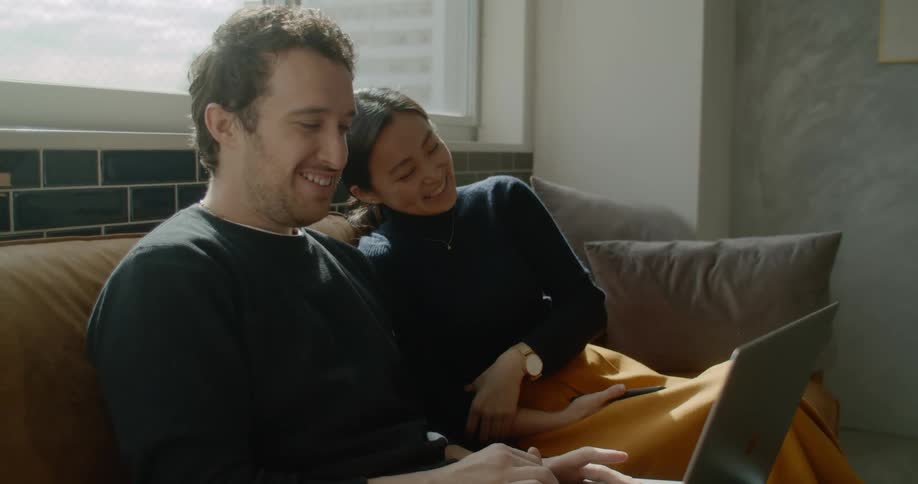 Couple sitting on couch laughing and looking at laptop