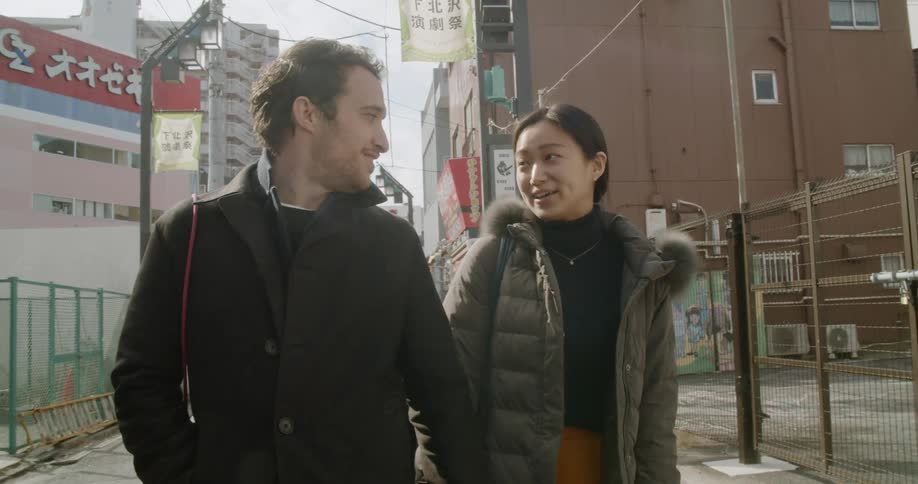 A man and woman walk down a city street holding hands
