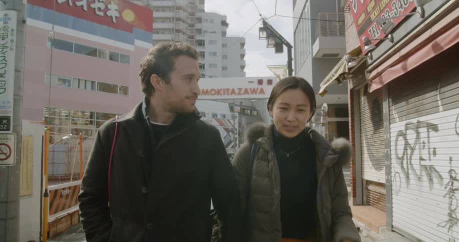 A man and woman smile and laugh while holding hands on a city sidewalk