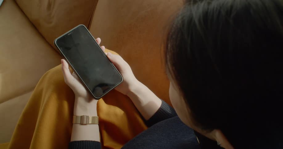 A woman sits on a couch and looks at a smart phone