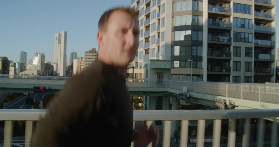 A man jogs across an overpass above a highway in a large city