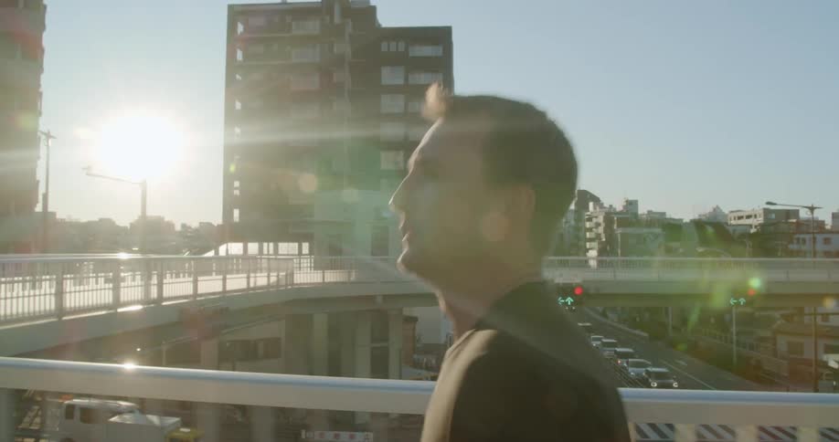 A white man jogs on an elevated walkway through a city downtown