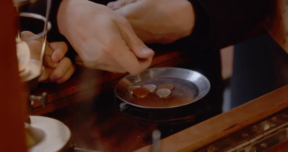 A person counts out and places several coins on a plate on a glass top counter