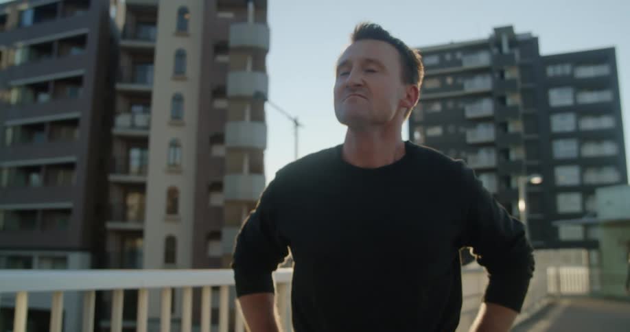 A man straightens up and takes a deep breath outdoors