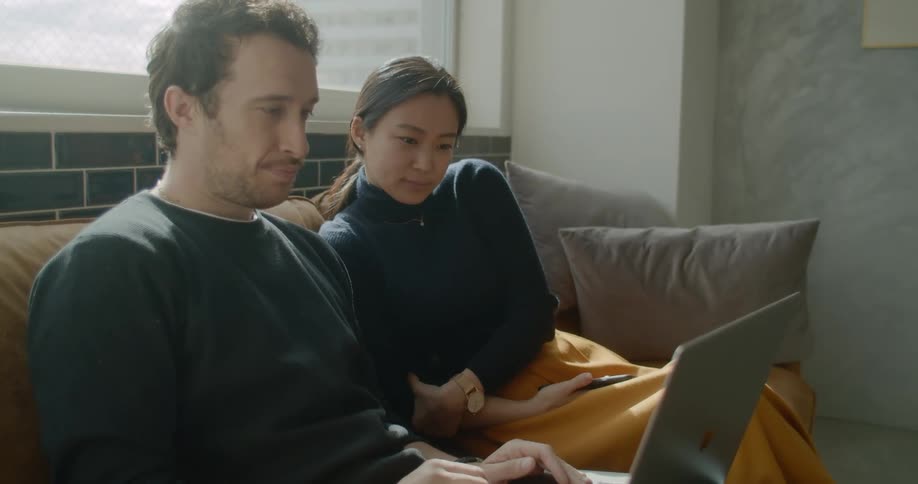 Man and woman sit together on sofa looking at laptop