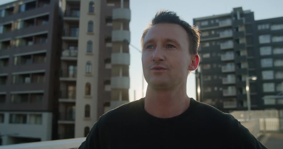 A man stands with his hands on his hips and breathes deeply while standing on a city street