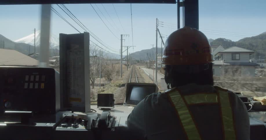 A train operator with a hard hat and vest operating a train