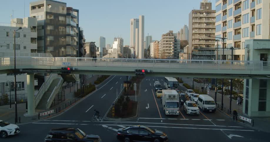 Vehicles driving through a busy intersection while pedestrians walk across a bridge overhead