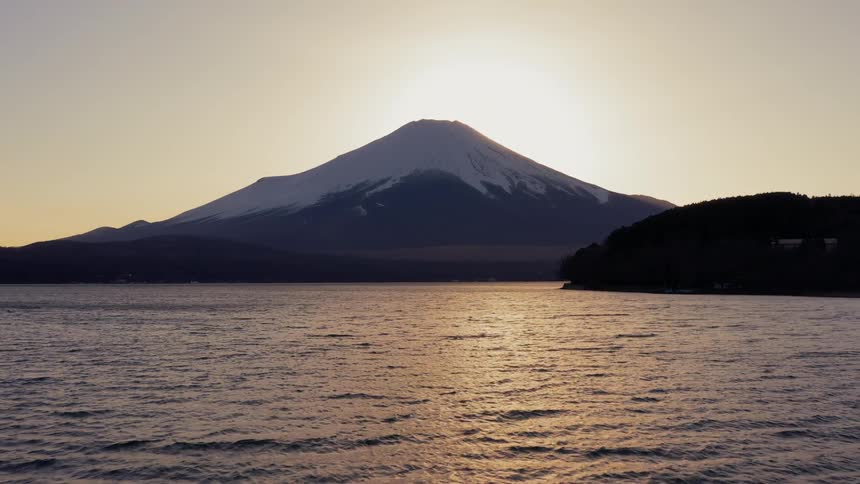 A lake flows in front of a mountain at sunset