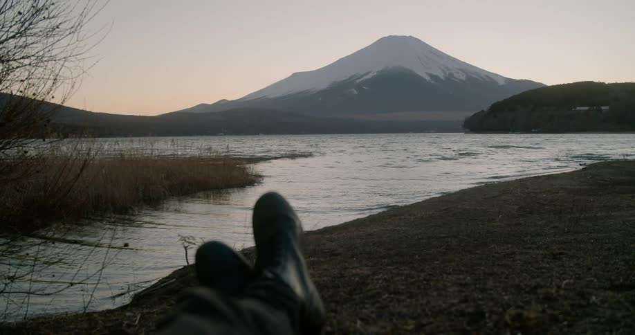 A person crosses their legs as they lay on the ground and look at mount fuji at sunset