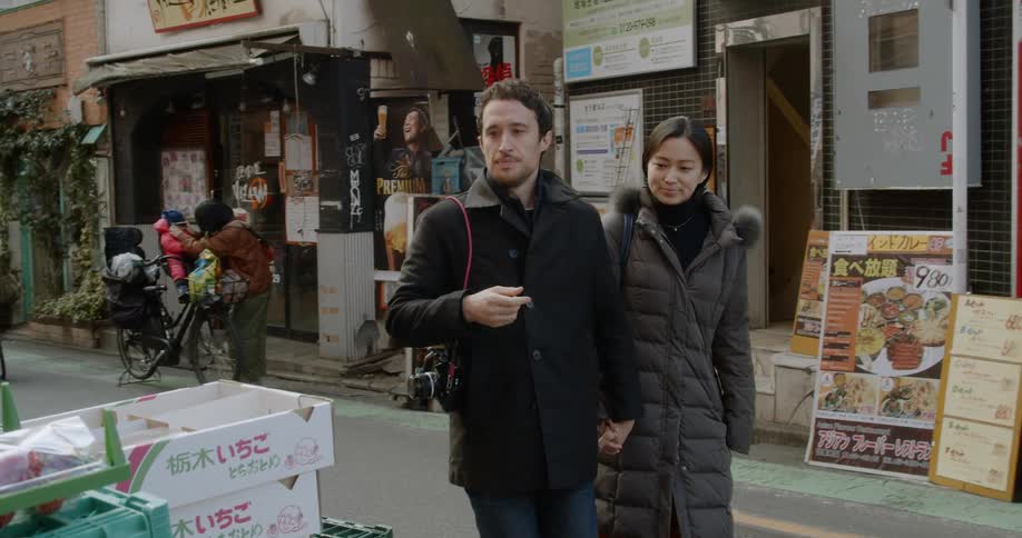 Couple walks through street stopping to examine fruit at store