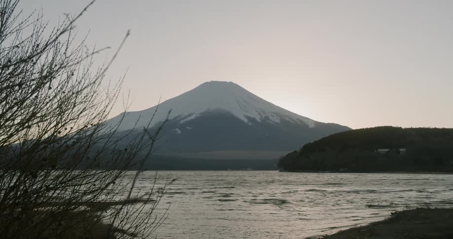 Wind blowing bare branches and rippling the water surface with a snow capped mountain peak on the horizon