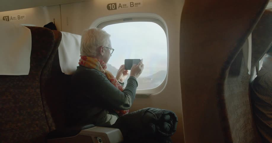 Older woman on train takes photo through window