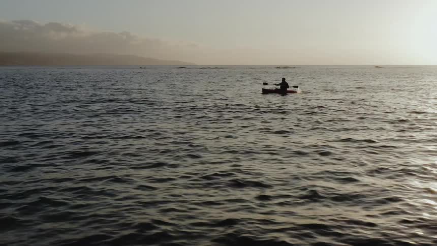 Man paddles across rippling water as sun rises over the horizon