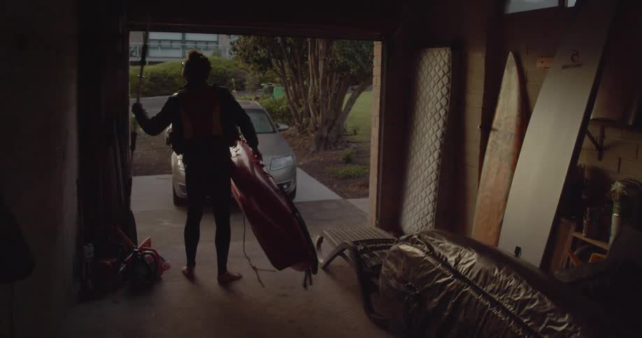 Man picking up then carrying kayak and paddle out of garage in early morning