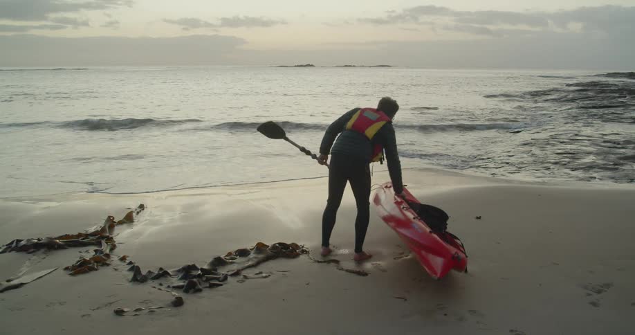 A man carries a kayak and oar towards the ocean water