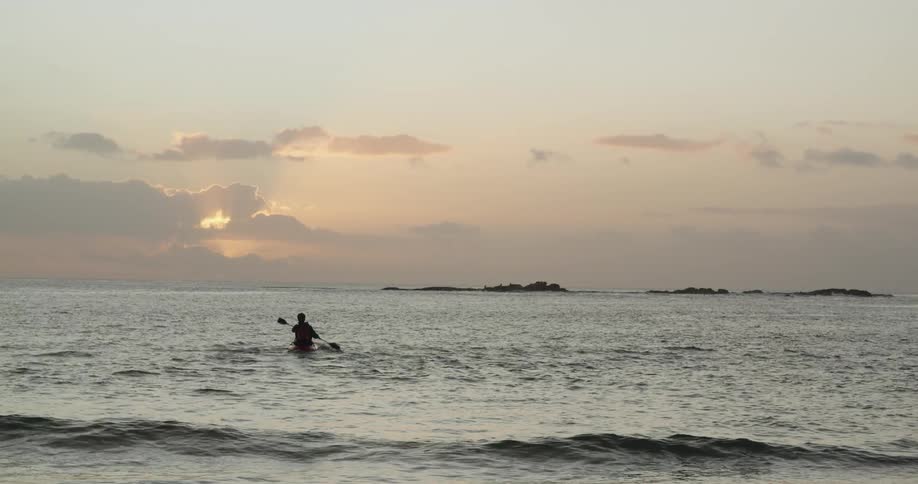 The silhouette of a person kayaking on the waves at sunset