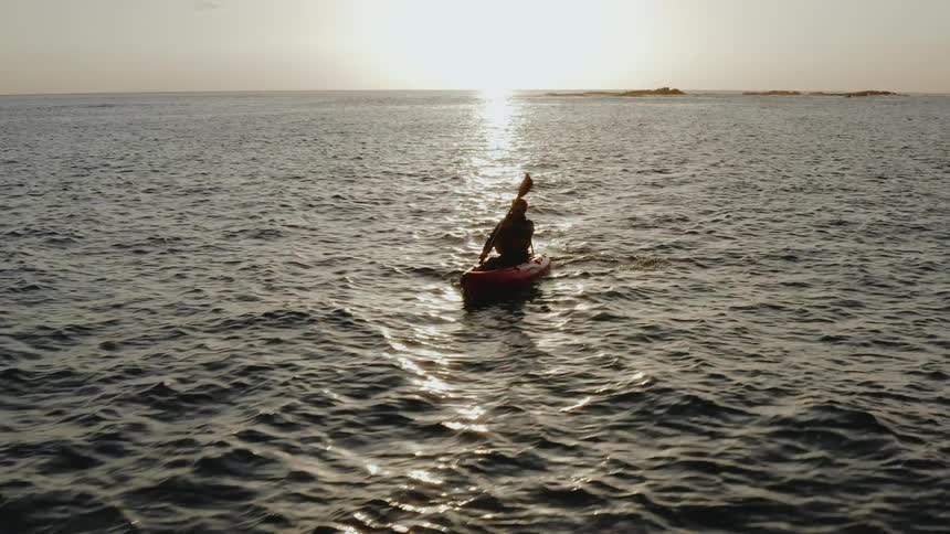 Man rows a kayak on calm waters at sunrise