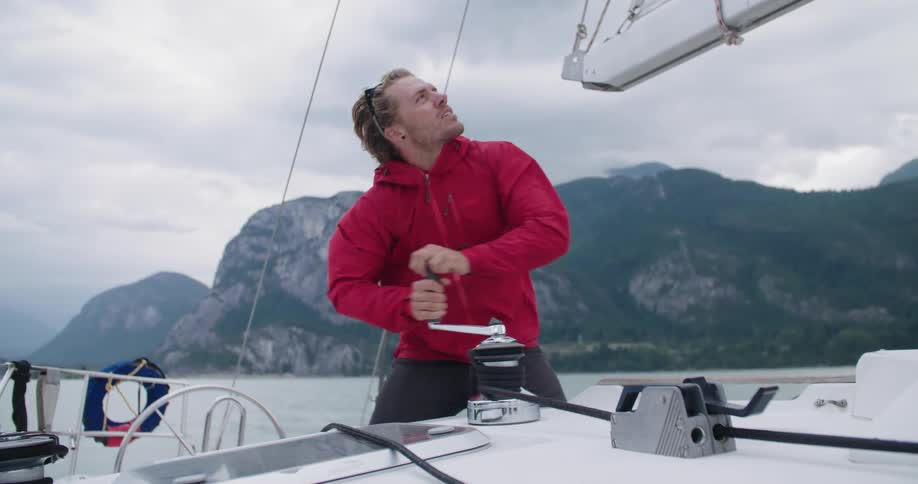Male turns the winch on a boat out on the water and looks up to keep an eye on the sail