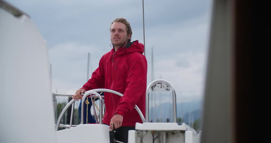 A man is steering a boat while wearing a red jacket