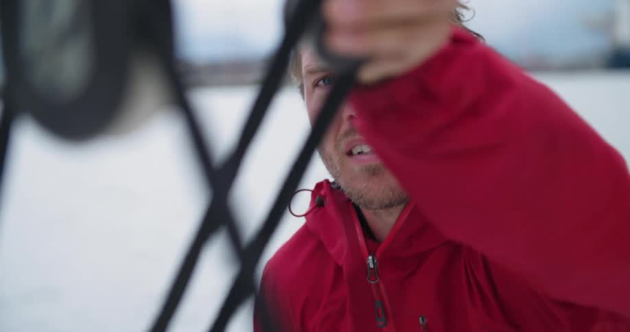 Man wearing a red jacket reaches up and twists some black cables