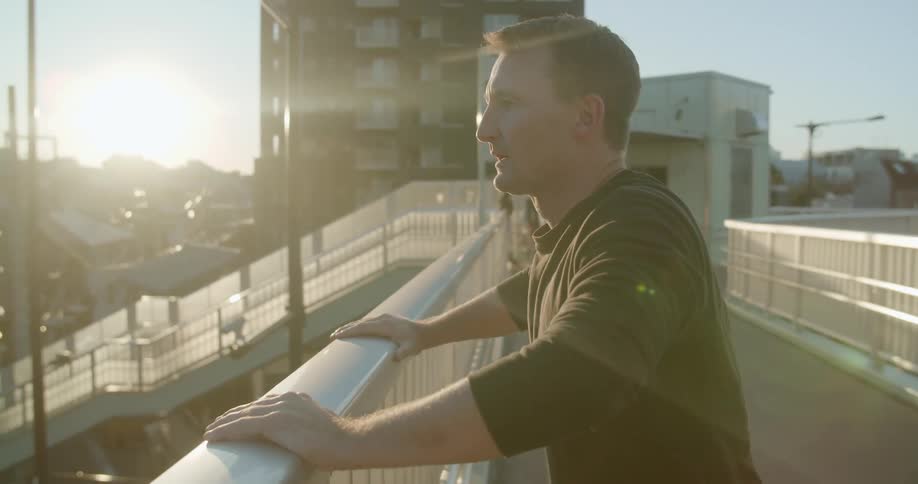 A white man leans against an outdoor railing while taking deep breaths
