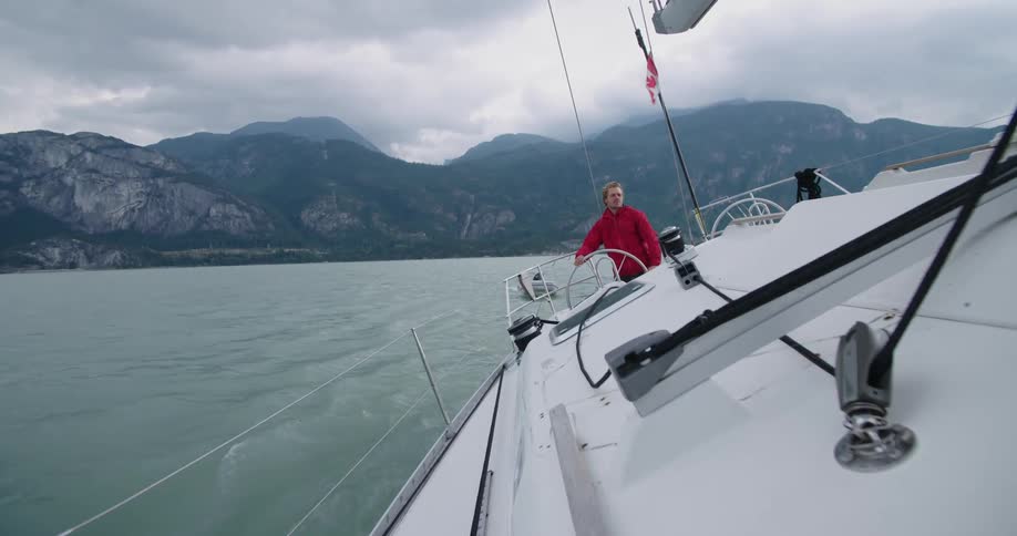 A man steering a yacht with mountains in the background
