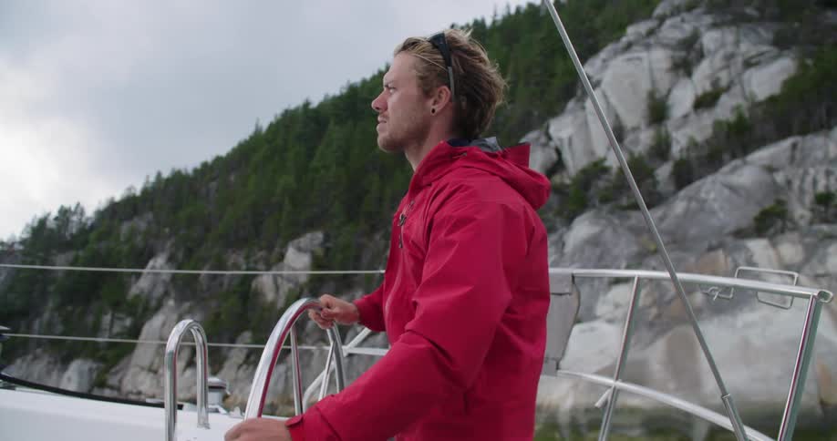 A man stands on deck and turns the ships wheel as the wind blows