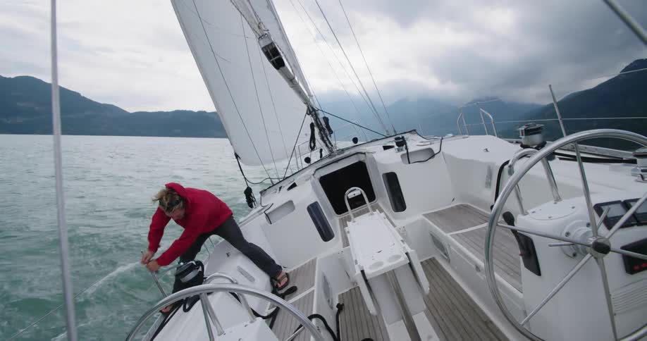Man coiling rope on sailboat speeding on the ocean near mountains