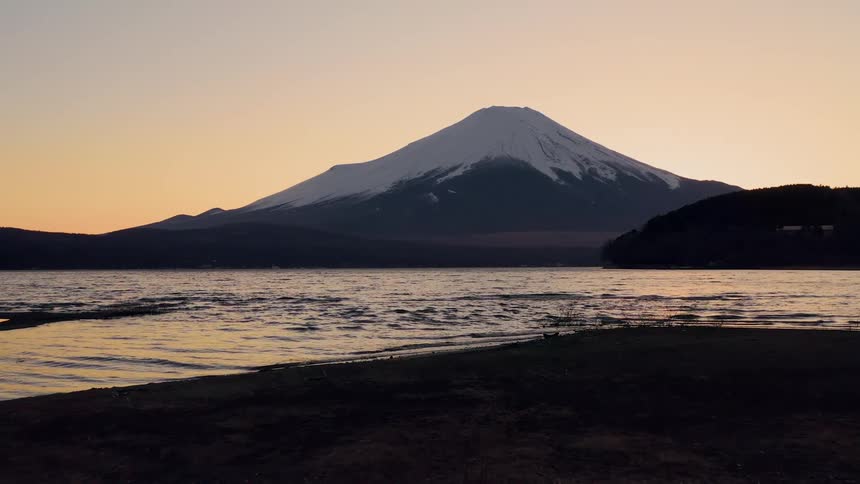 A man stands by a river looking at a mountain in the distance