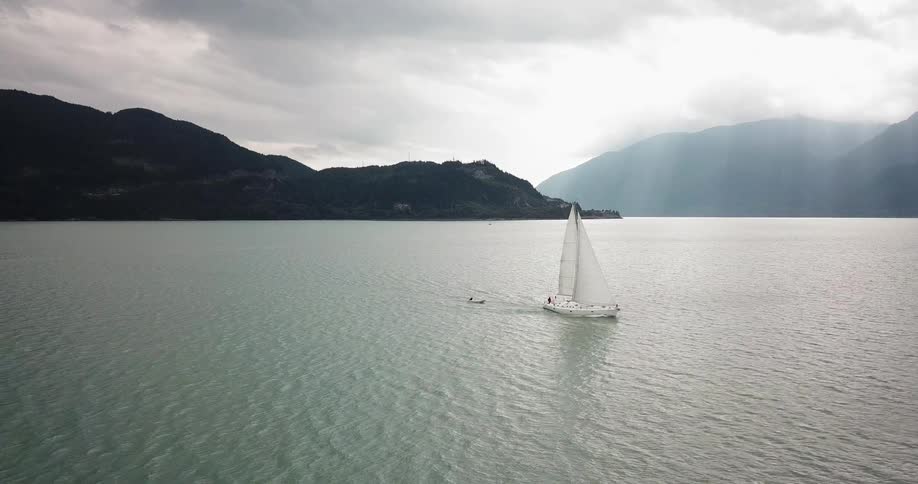 A sailboat tows a smaller vessel on a lake